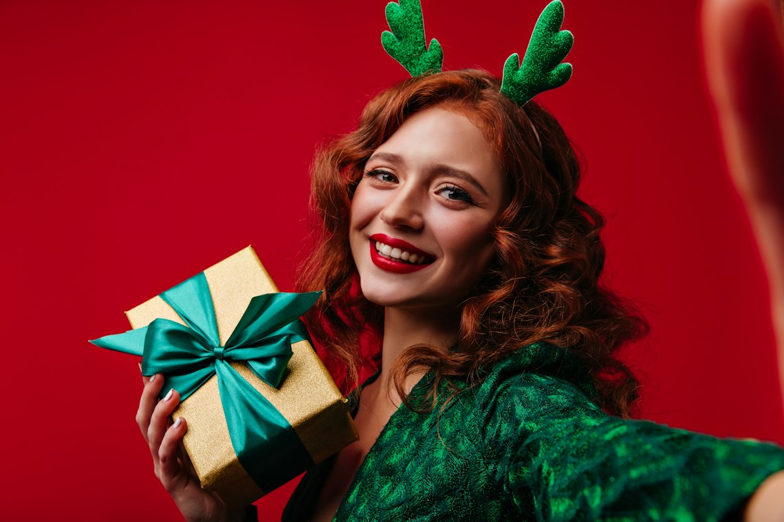 Smiling woman in festive antlers holding a Christmas gift